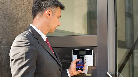 Staff member uses door entry system with mobile device to enter office building 